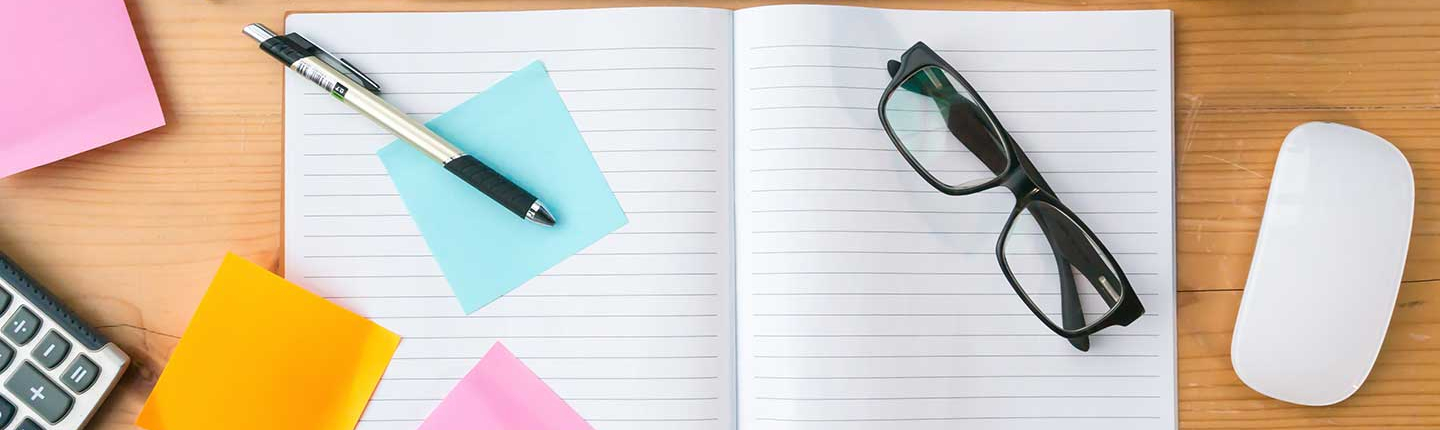 top-down view of an organized wooden office desk with various items including a keyboard, mug, notebook and colorful sticky notes