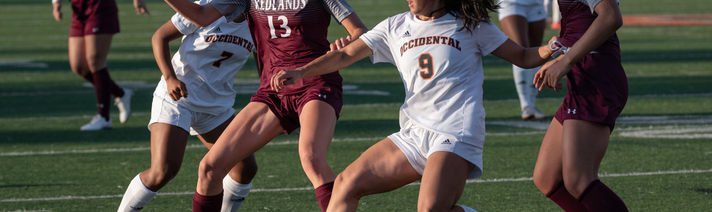 Four women playing soccer on turf field during daylight