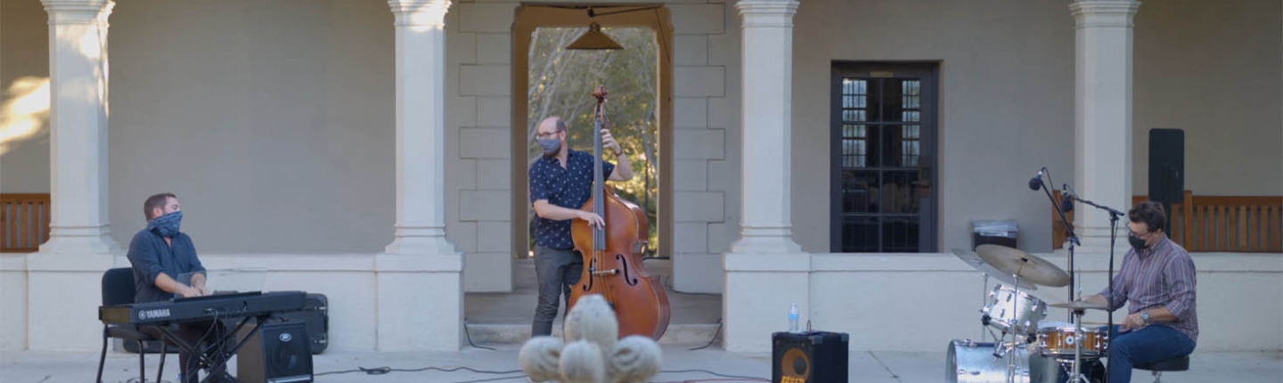 A jazz trio of piano, bass, and drums performing in the Booth Hall courtyard