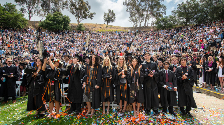 Occidental students standing in black caps and gowns in the Remsen Bird Hillside Theater, celebrating