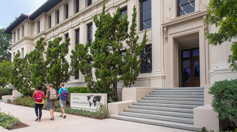 A view of the front of Johnson Hall with three students passing on the sidewalk
