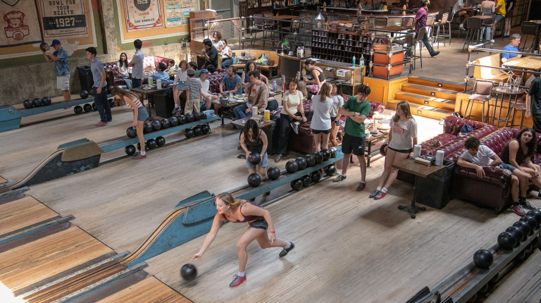 A large group of students bowling at a steampunk-themed bowling alley