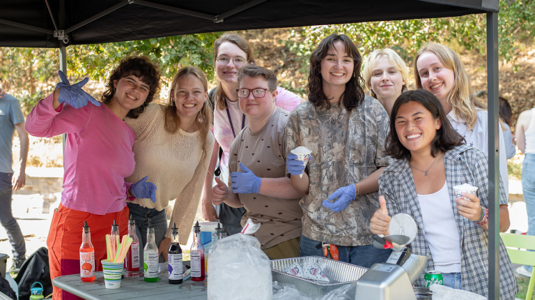 A happy group of Occidental College students posing together at a snow cone assembly table