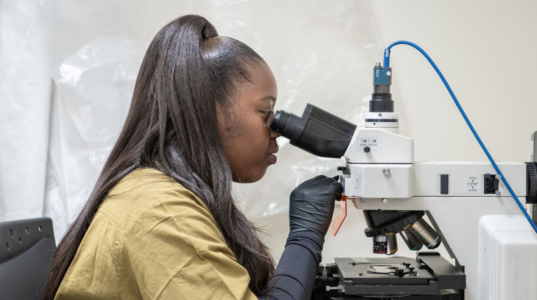 Daisy Ademoye looking into a powerful microscope in the Mind and Brain lab