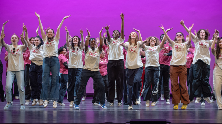 Oxy students on stage, arms up and smiling as they perform in Dance Pro