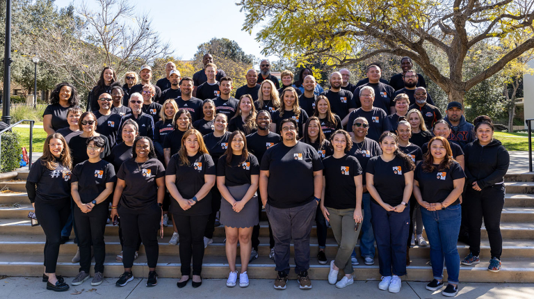 A large group of Student Affairs staffers standing on the steps on campus in black tshirts