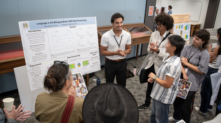 a group of Occidental College students stands around a male student giving a poster presentation about his research