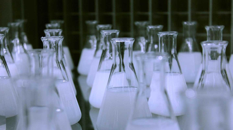 Rows of mostly full chemistry flasks with shadowy light, representing the chemistry department at Occidental College (Oxy).