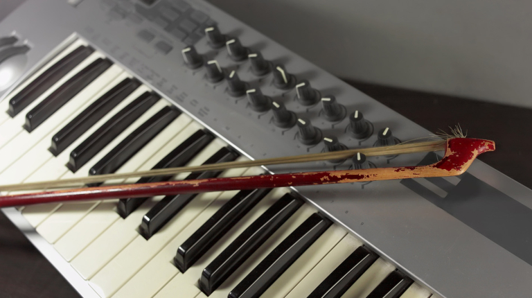 an electronic keyboard controller with a violin bow resting on its keys