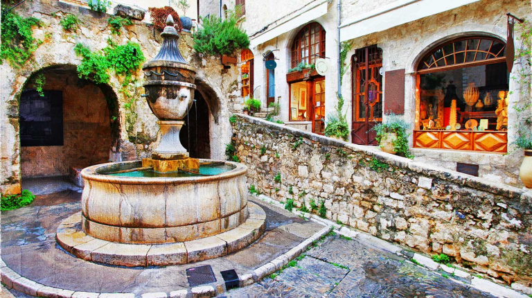 a picturesque street scene featuring the Place de la Grande Fontaine in the medieval hilltop village of Saint-Paul-de-Vence on the French Riviera. 