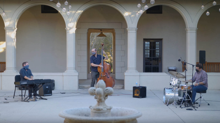 A jazz trio of piano, bass, and drums performing in the Booth Hall courtyard