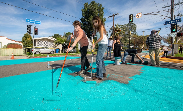 Two students painting the asphalt on Yosemite Way a bright teal color