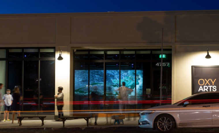 People stand in front of the Oxy Arts building at night, wit