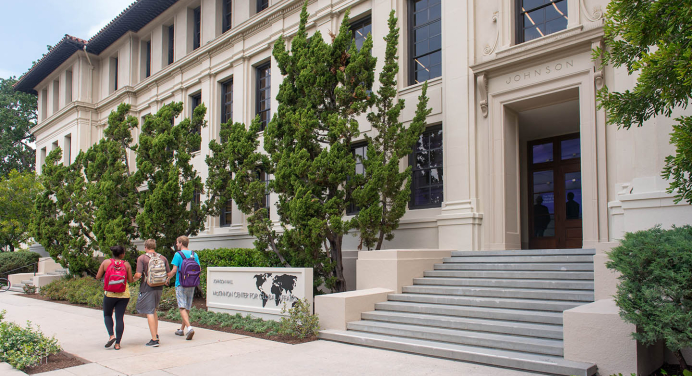 A view of the front of Johnson Hall with three students passing on the sidewalk