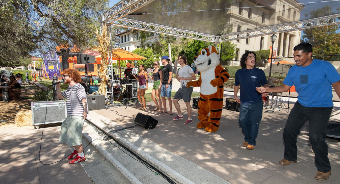 Occidental College students dancing in a group on campus with Oswald the Tiger