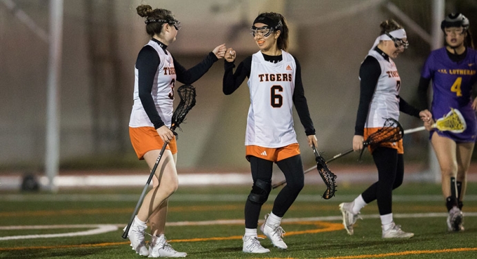 Two Oxy students playing women's lacrosse fist-bump each other