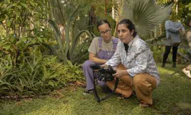Anahid Yahjian, right, a female Armenian director crouching down with a coworker in a green outdoor setting