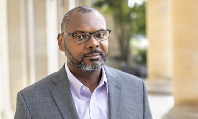 Professor Derrick Spires headshot with glasses and grey coat