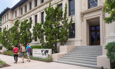 A view of the front of Johnson Hall with three students passing on the sidewalk
