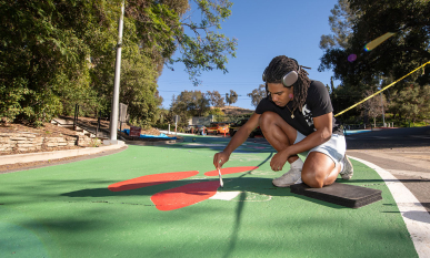 An Occidental College student paints a mural on a road on upper campus