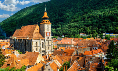 A quaint Romanian village with orange-colored roofs and a steeple in the middle against a lush green hillside