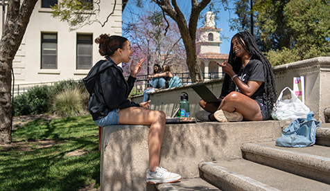 Two Occidental (Oxy) students seated on stone steps on a green campus