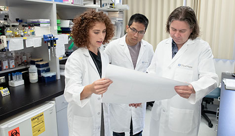 three people in a laboratory setting, looking at a document together