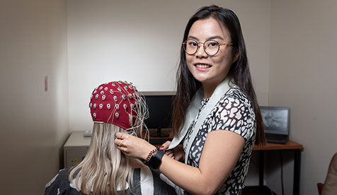 An Occidental student in a research setting where an individual's brain activity is being measured using an EEG cap