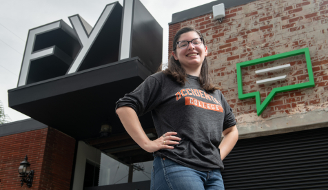 Occidental student standing in front of an office with a sign reading "FYI"
