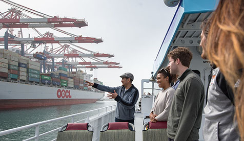 Occidental students standing on a boat next to a shipping boat