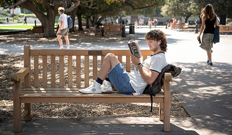 An Occidental student leaning on a bench, reading a book at the Oxy Quad