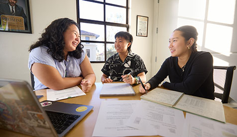 Three Occidental (Oxy) students seated at a table covered with papers discussing coursework