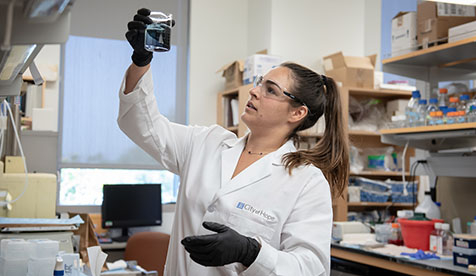 An Occidental College student working at City of Hope doing medical research, holding a beaker up to the light