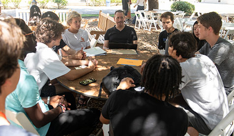 Group of oxy students sitting around a circular wooden table outdoors