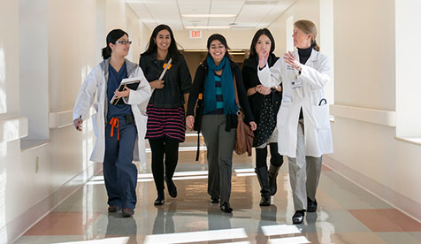 A group of Occidental (Oxy) students and a professor walking down a hallway. Two are wearing lab jackets and 3 are wearing street clothes