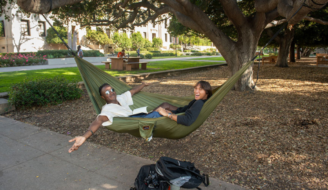 Two Occidental Students sitting in a hammock with their arms outstretched