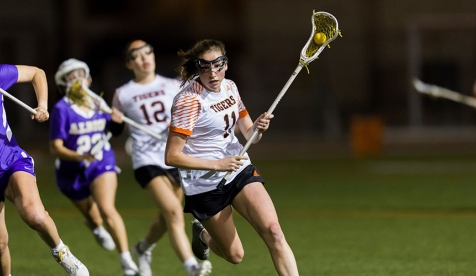 Occidental College women's lacross players running across a green field at a night game