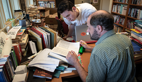 Teacher and student look at textbook together, surrounded by other books.