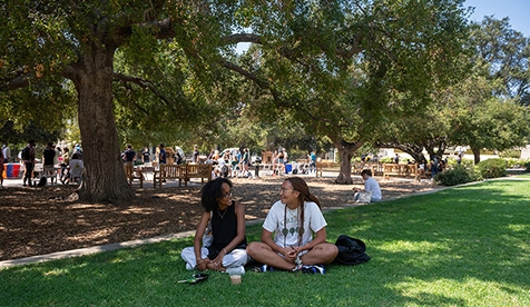 2 students sit on grassy lawn near quad