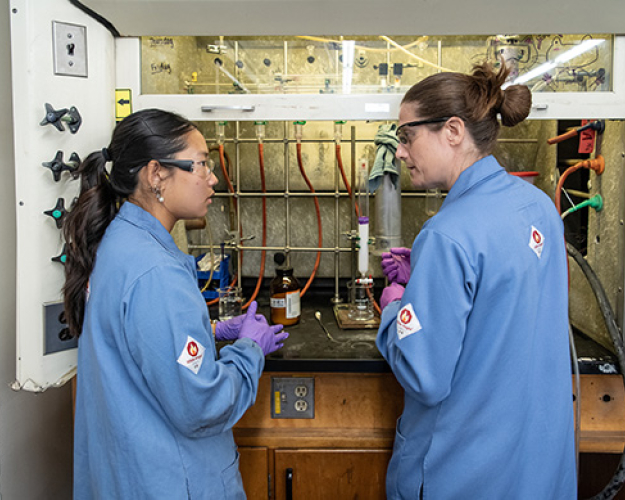 Two people in a lab setting, wearing blue jackets