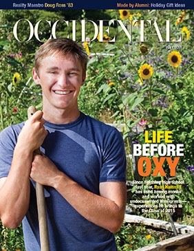 A young man with a shovel stands smiling in front of a garde