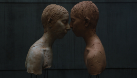 color image of two sculptural human busts in profile with faces touching