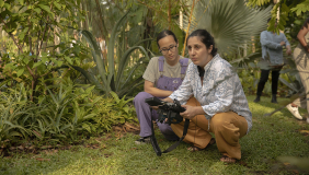 Anahid Yahjian, right, a female Armenian director crouching down with a coworker in a green outdoor setting