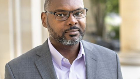 Professor and author Derrick Spires headshot wearing a grey sports coat and glasses