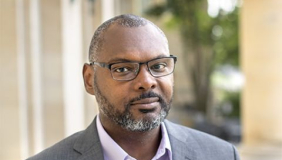 Professor and author Derrick Spires headshot wearing a grey sports coat and glasses