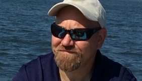 Man with hat and sunglasses in front of water