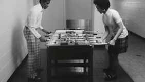 Black and white photograph of two Black people playing foosball 