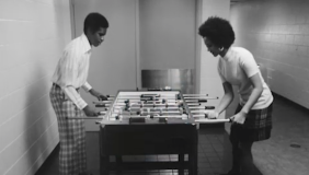 Black and white photograph of two Black people playing foosball 