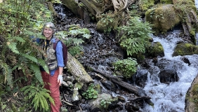 Dr. Greta Binford on a hillside with plants and a stream