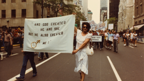 Archival image of Sylvia Rivera walking in a protest holding a large banner 